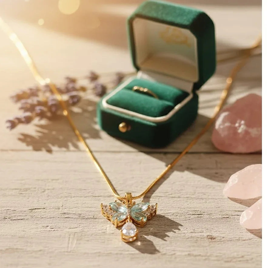 Gold necklace with butterfly pendant on a wooden surface with a green jewelry box.