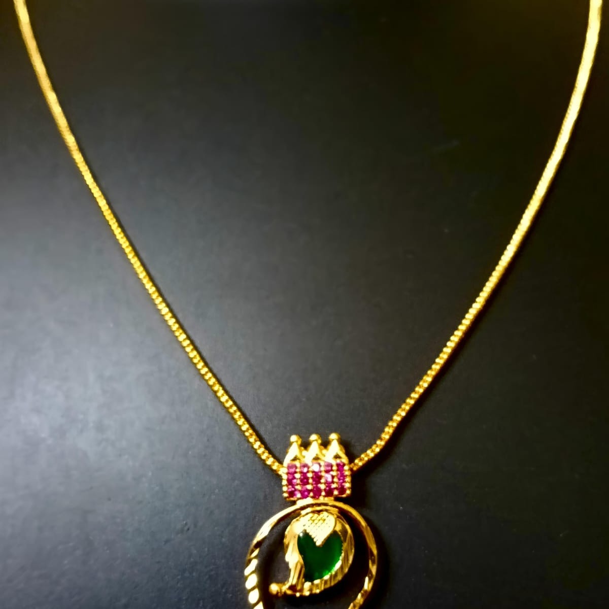 Gold necklace with a pendant featuring a green gemstone and pink accents