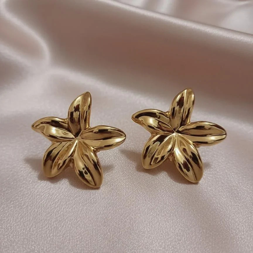 Pair of gold flower-shaped earrings on a satin surface