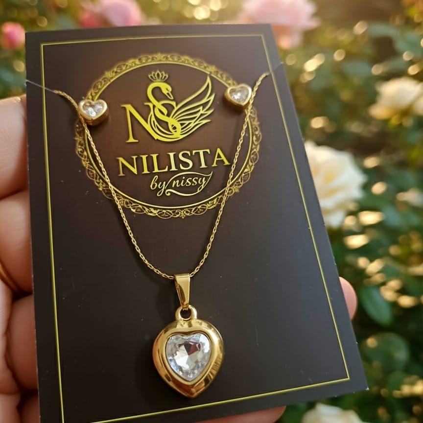 Gold necklace with heart-shaped pendant on a Nilista by Nissy card, held against a blurred floral background.