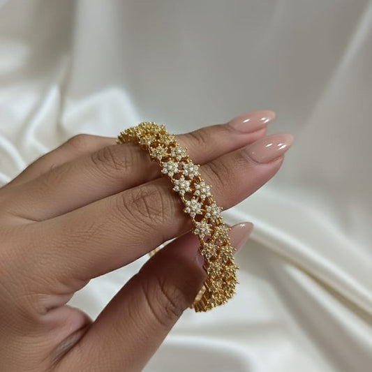 Gold beaded bracelet on a hand against a neutral background