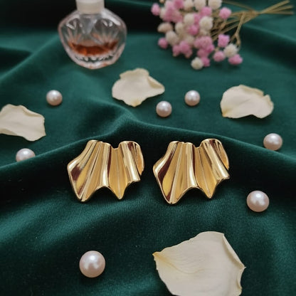 Gold earrings on a green fabric background with pearls and flowers.