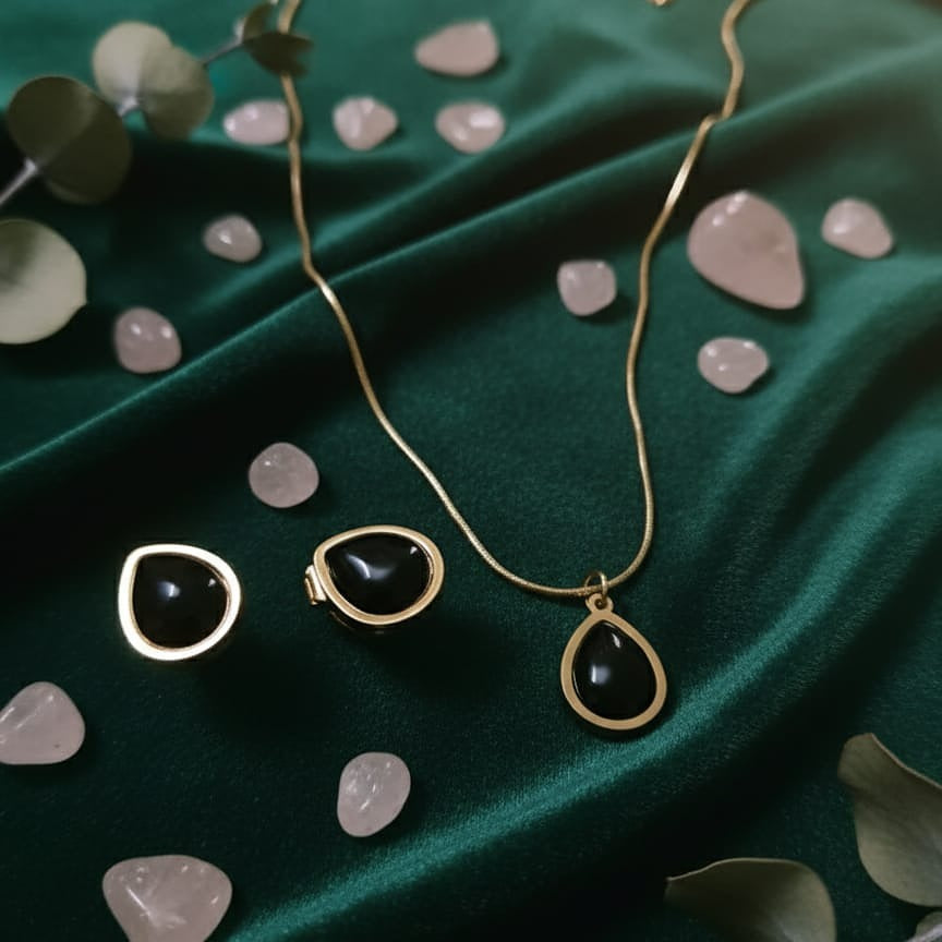 Gold necklace with black teardrop pendants on a green fabric background with stones and leaves.