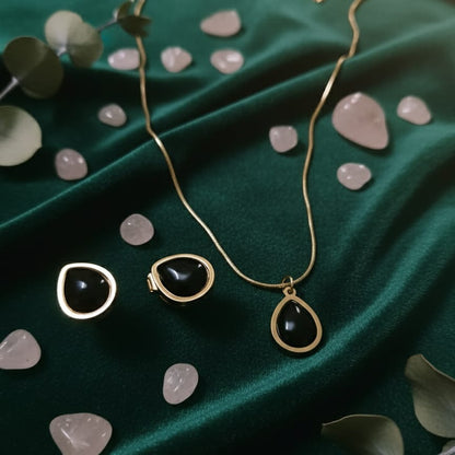 Gold necklace with black teardrop pendants on a green fabric background with stones and leaves.