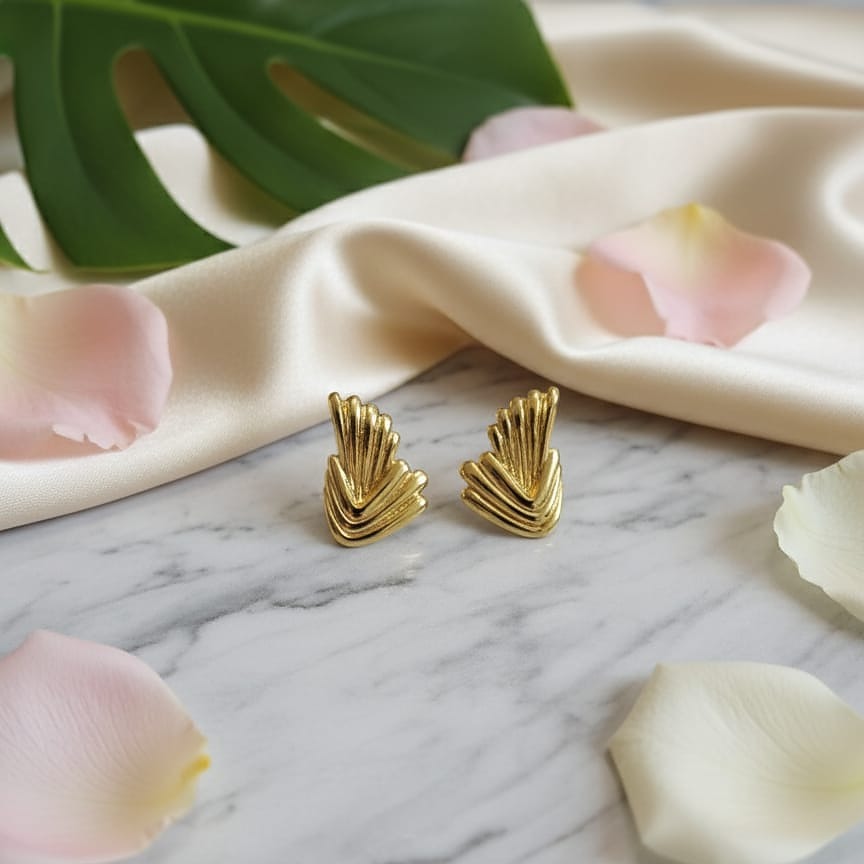 Gold earrings on a marble surface with pink petals and green leaves