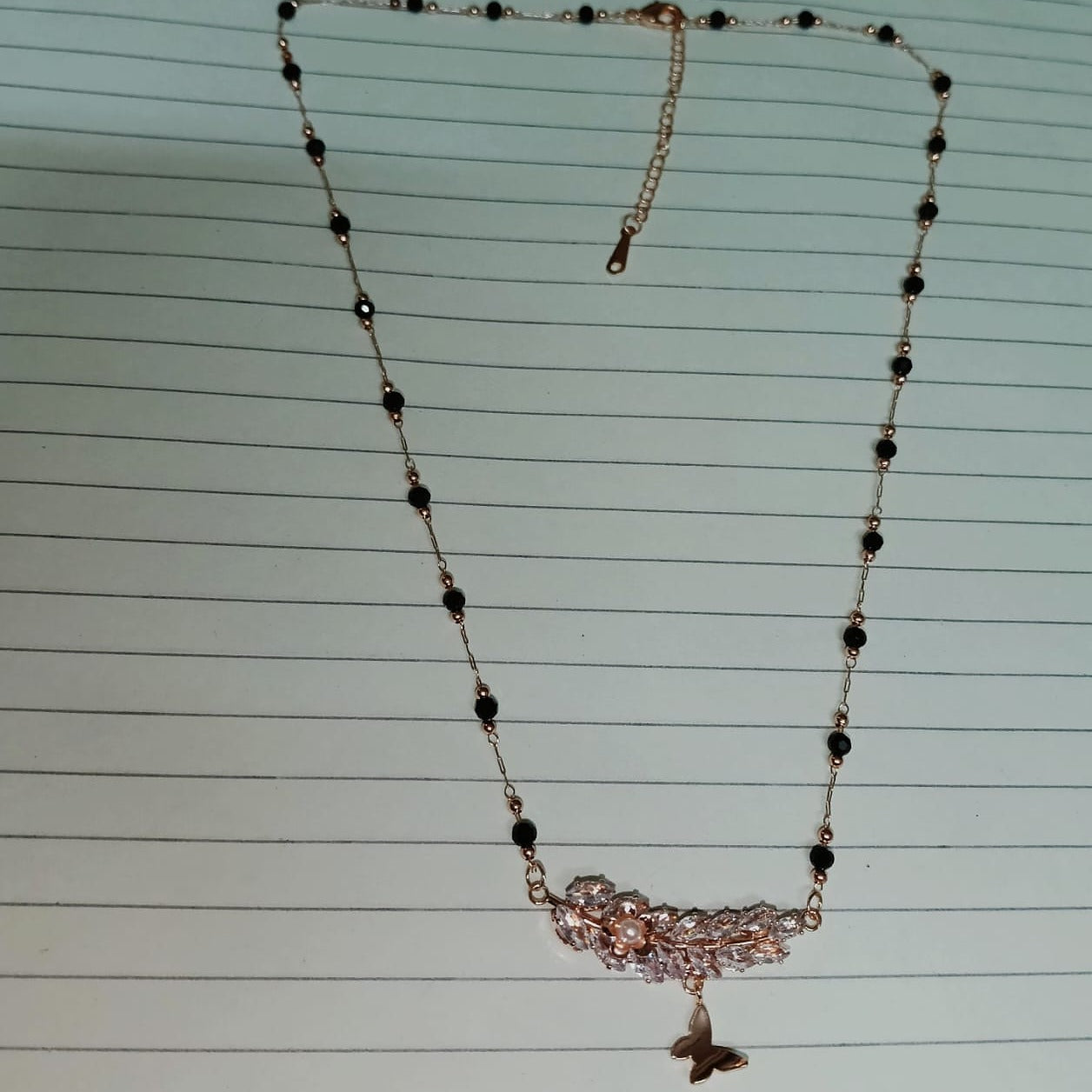 Necklace with black beads and a butterfly pendant on lined paper