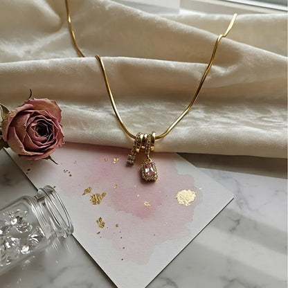 Gold necklace with pink charms on a marble surface with a pink rose and card.