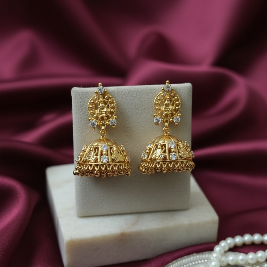 Gold earrings on a white stand with a maroon fabric background