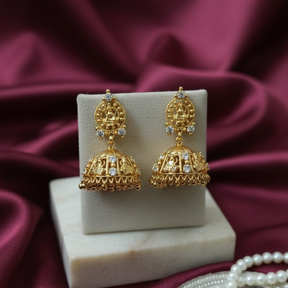 Gold earrings on a white stand with a maroon fabric background