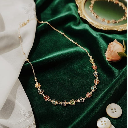 Necklace with colorful beads on a green velvet surface with a white fabric and buttons in the background.