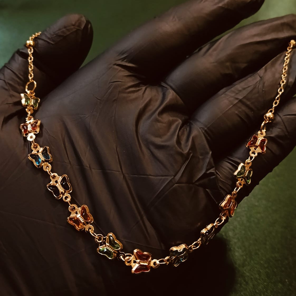 Gold chain with colorful pendants held by a gloved hand on a dark background