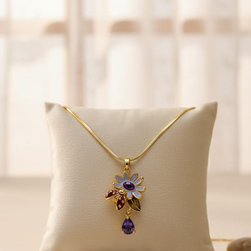 Gold necklace with a floral pendant featuring purple and red gemstones on a beige pillow.
