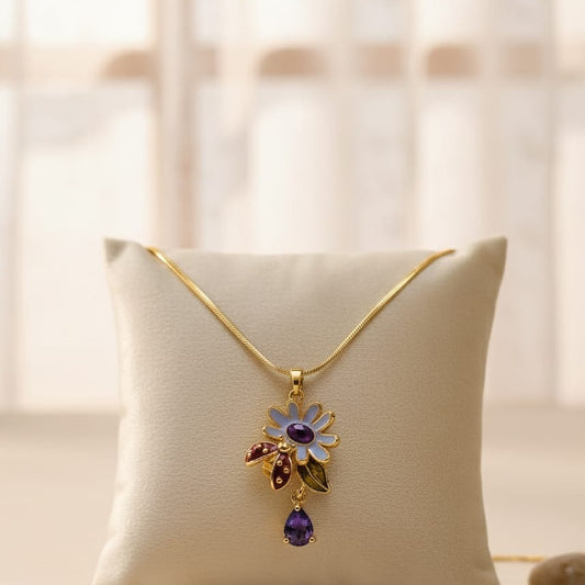 Gold necklace with a floral pendant featuring purple and red gemstones on a beige pillow.
